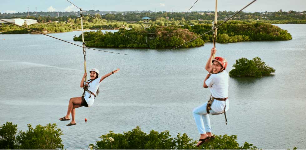 Imagem de duas mulheres fazendo tirolesa por cima de um rio.