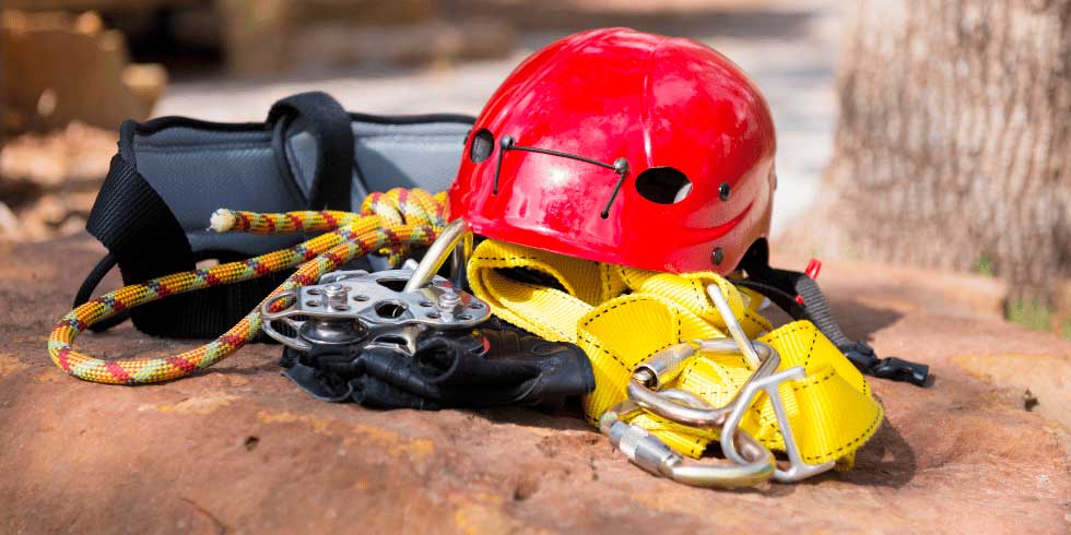 Equipamentos da tirolesa, como capacete, mosquetões e banco juntos em uma pedra